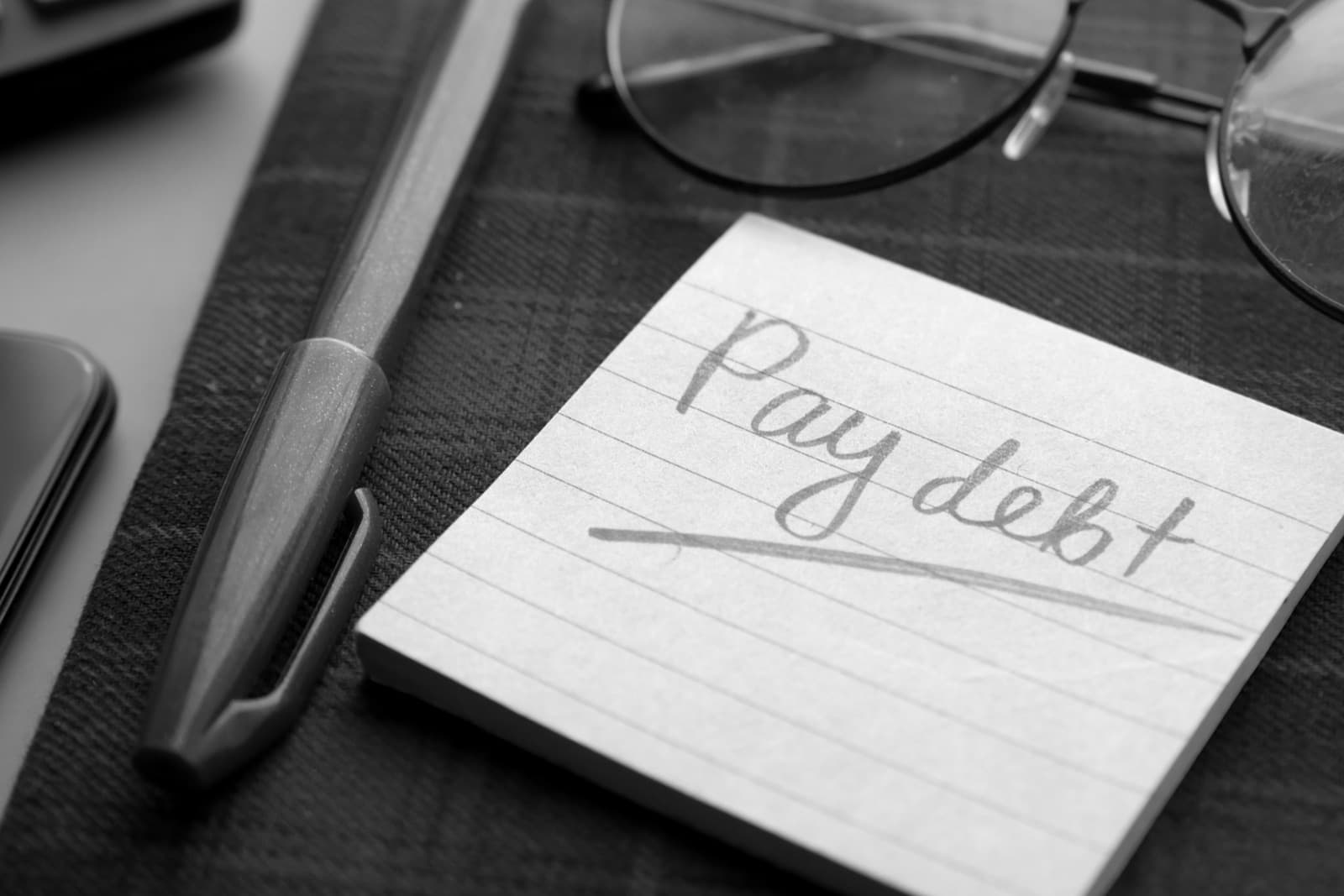 紙上寫住「Pay debt」嘅便條，旁邊有眼鏡同筆