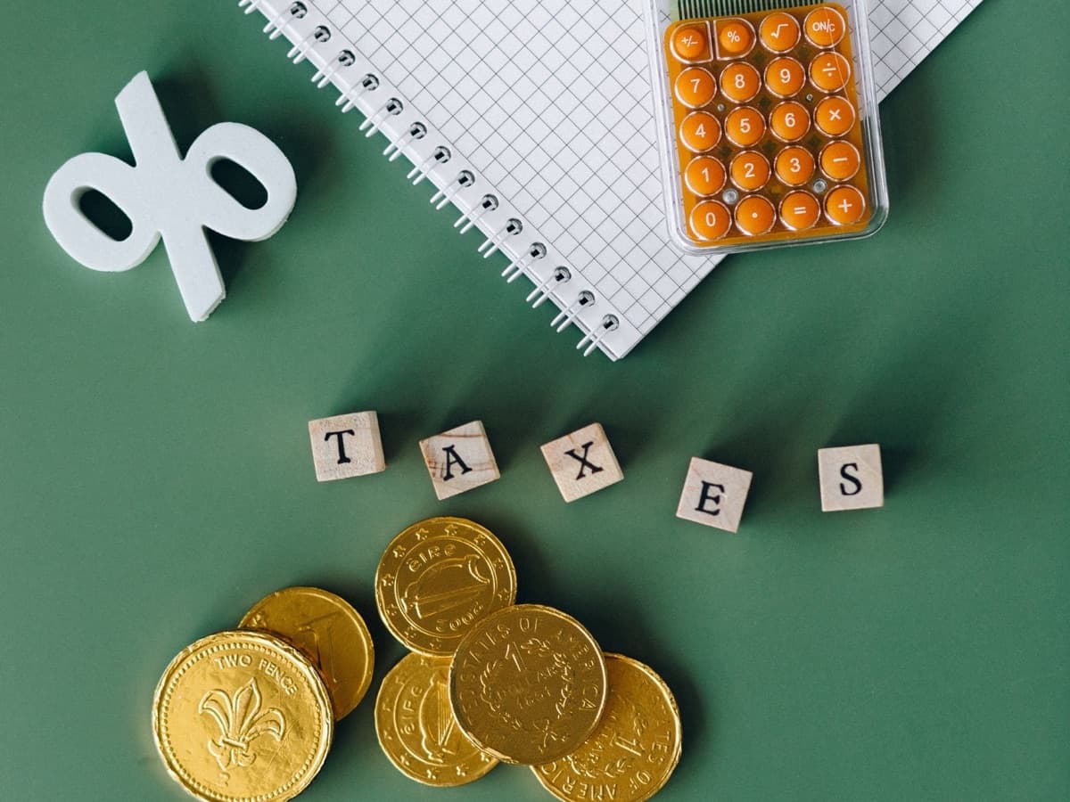 綠色桌面上面嘅筆記簿、計算機同硬幣,旁邊放住「TAX」字樣方塊